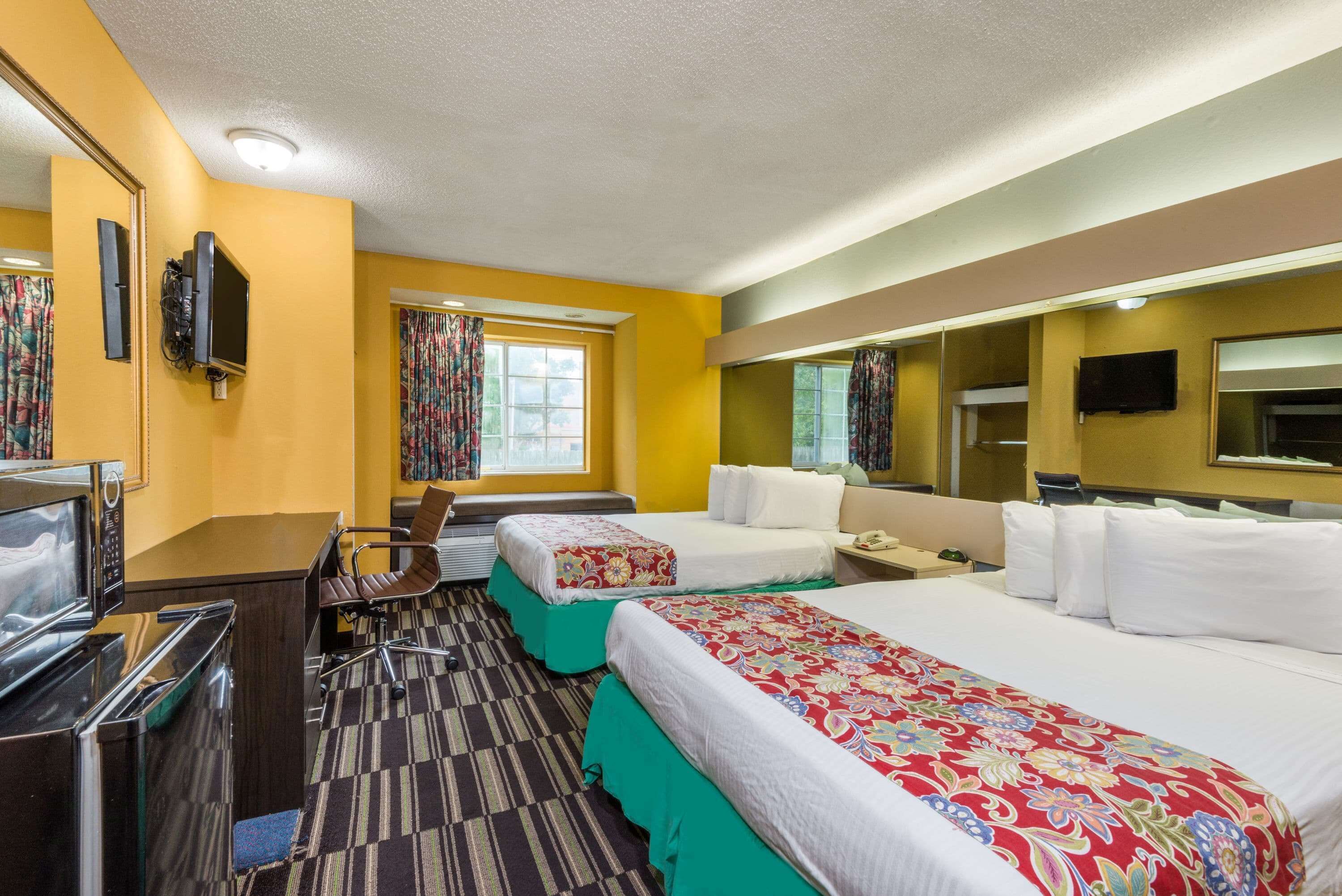 A hotel room with two beds, a desk with a computer, a microwave, a telephone, and a television.