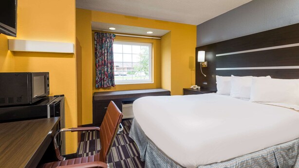 Une chambre d’hôtel avec un grand lit, un bureau avec un ordinateur, une télévision et une fenêtre avec des rideaux.