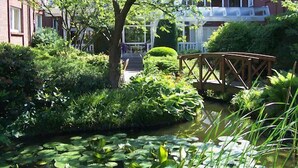 Ein Garten mit Teich, einer Holzbrücke und einem Gebäude mit Veranda im Hintergrund.