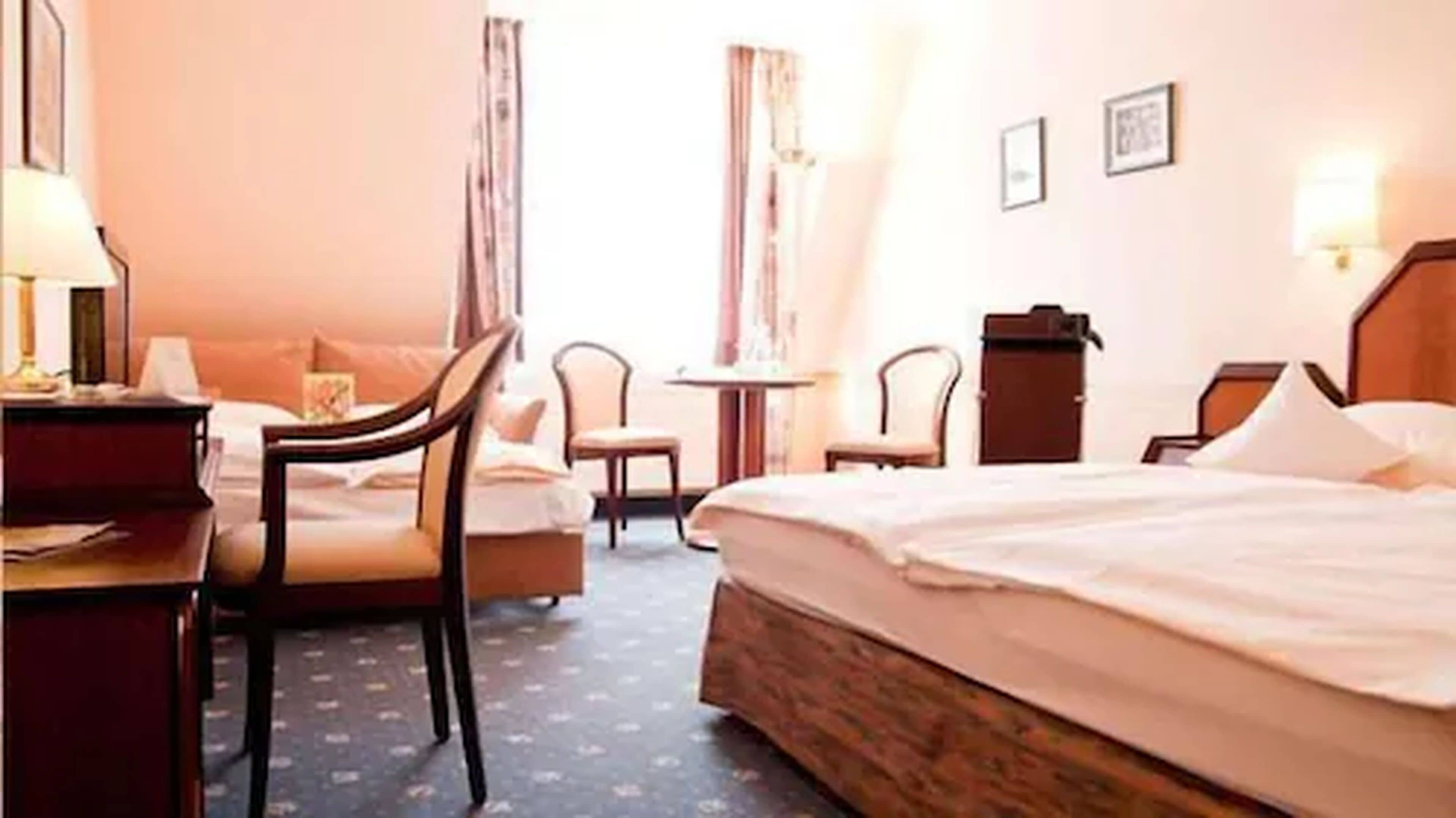 A hotel room with a bed, two chairs, a desk, a small table, and a lamp.