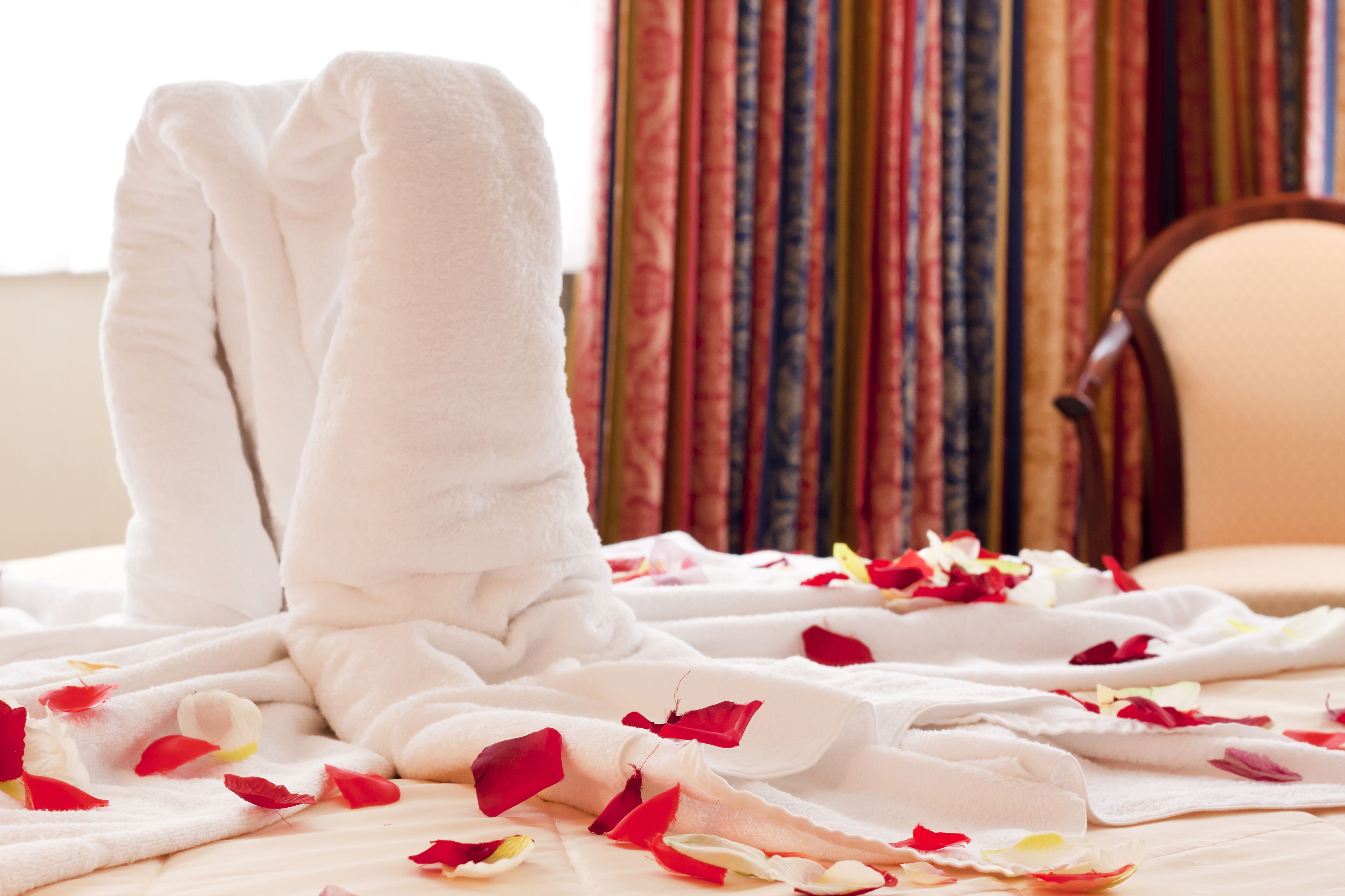 A bed with white towels and rose petals.