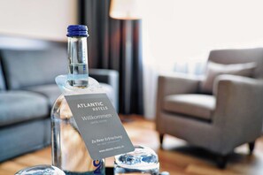 Alkoholipullo, jonka etiketissä lukee ”ATLANTIC HOTELS”, ja kortti, jossa on teksti ”tervetuloa” ja ”Zu Ihrer Erfrischung” (virvokkeeksi).