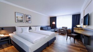 Ein Hotelzimmer mit einem großen Bett, einem Schreibtisch, einem Sessel und einem Fernseher.