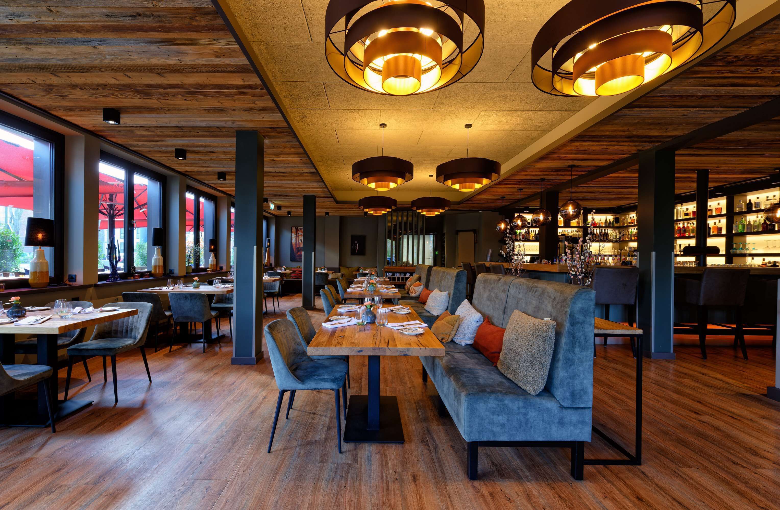 Un restaurante con suelos de madera, mesas redondas y asientos tapizados en gris.