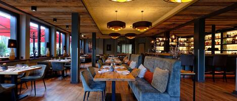 Un restaurante con suelos de madera, mesas redondas y asientos tapizados en gris.