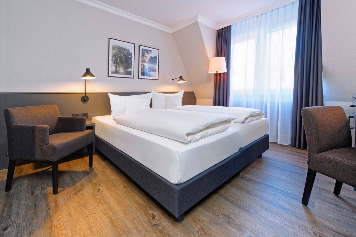 Habitación de hotel con una cama grande, dos sillones, un escritorio y una ventana con cortinas.