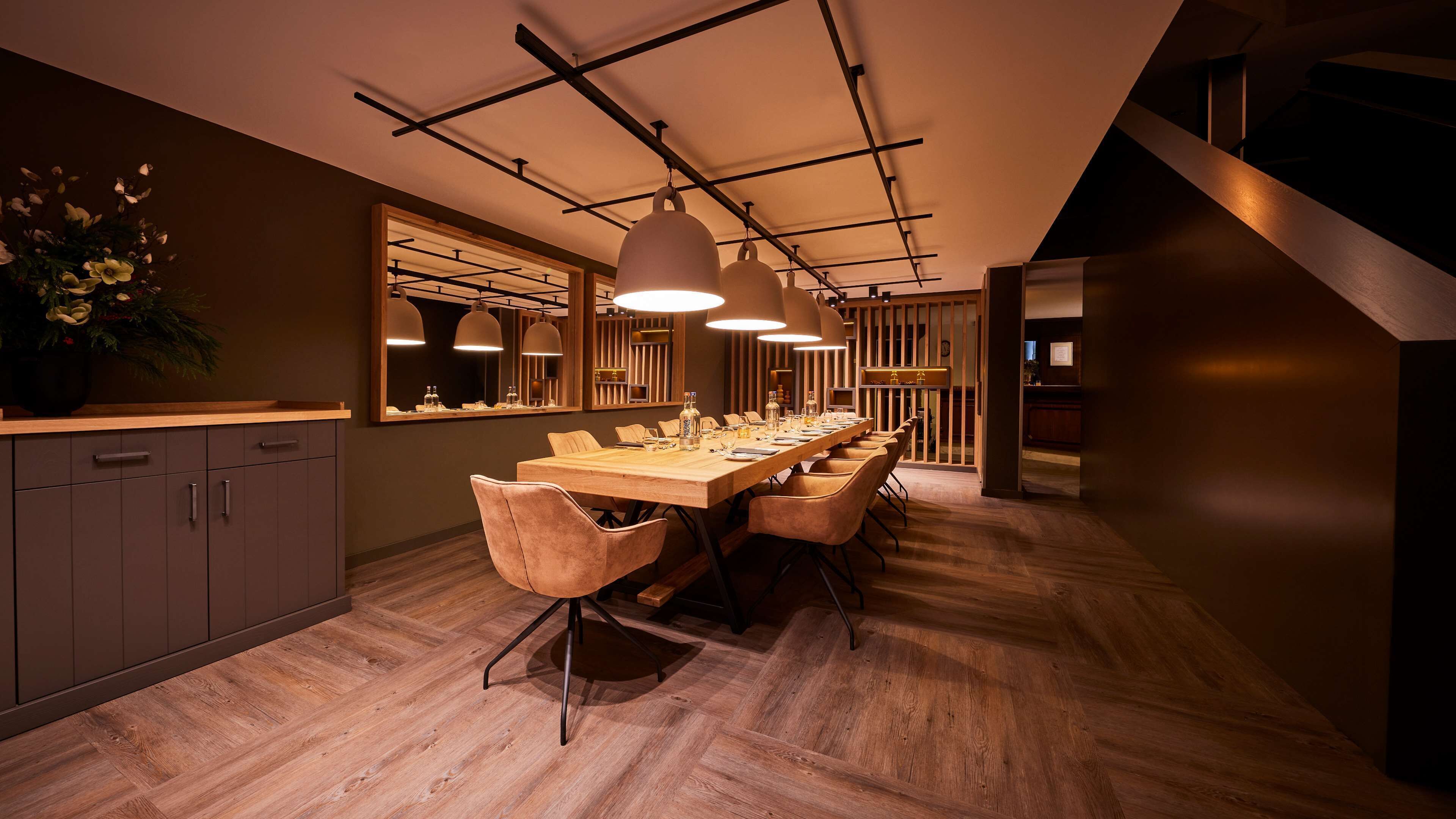 A modern dining area with a long wooden table, multiple chairs, pendant lights, and a large mirror.