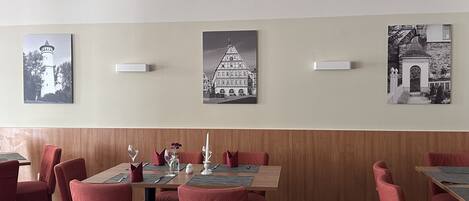 Un coin repas avec des chaises à revêtement rouge, une table en bois mise avec des couverts, et trois photographies en noir et blanc accrochées au mur.