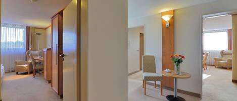 A hotel room with a bed, a desk, a chair, and a small table with a vase of flowers.