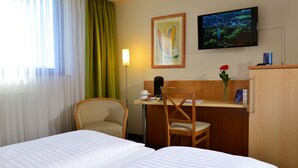 Habitación de hotel con dos camas, un escritorio con una silla, un televisor y un cuadro en la pared.