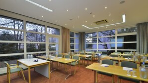 Un salón de conferencias con varias mesas y sillas, amplias ventanas y suelo alfombrado.