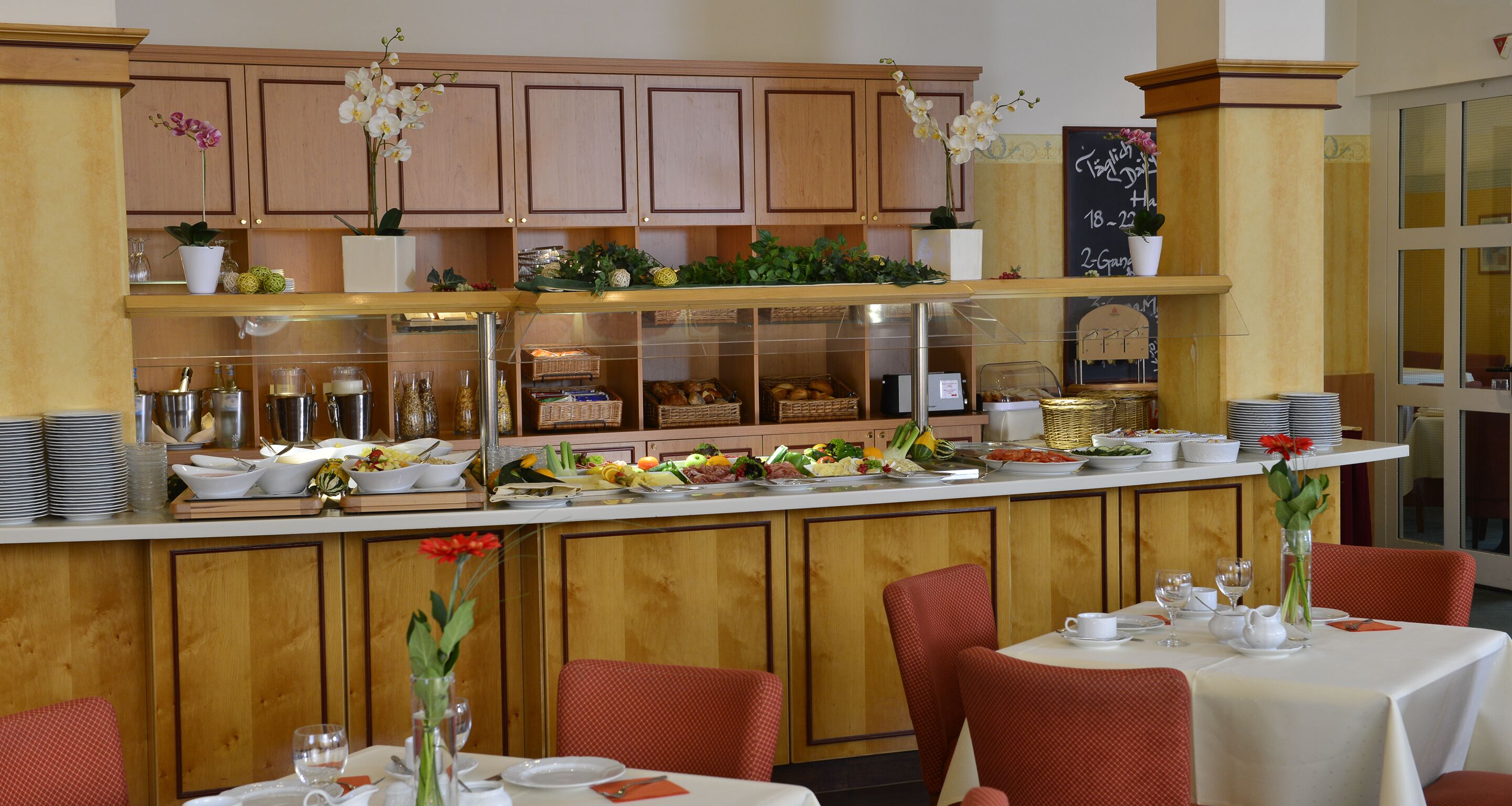 A restaurant with wooden cabinets, a buffet counter with various food items, and red upholstered chairs.