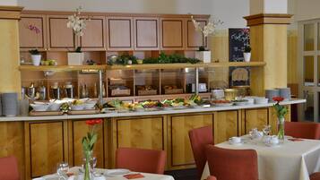 A restaurant with wooden cabinets, a buffet counter with various food items, and red upholstered chairs.