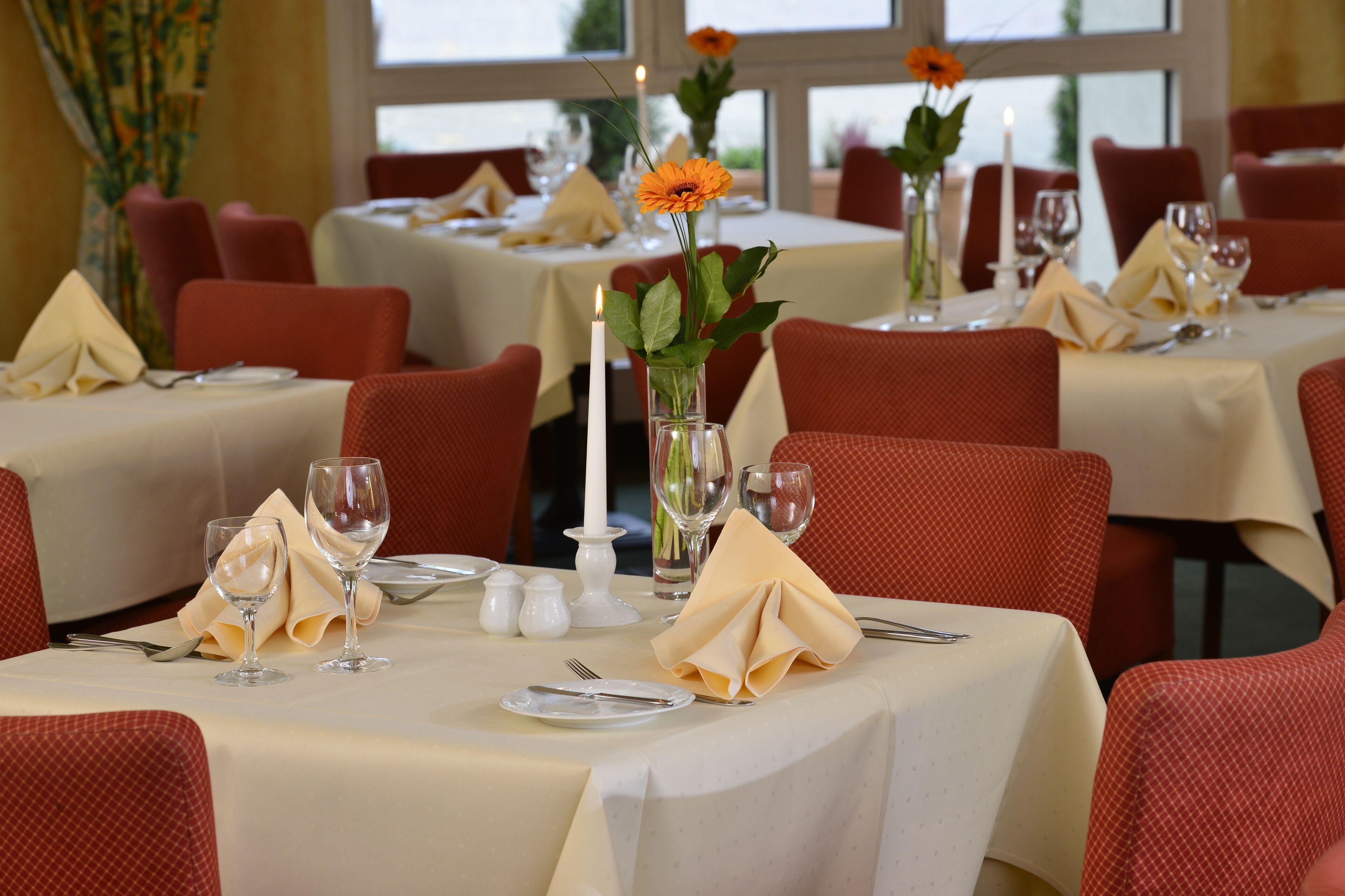 Ein Restaurant mit gedeckten Tischen, rote Stühle und weiße Tischdecken.