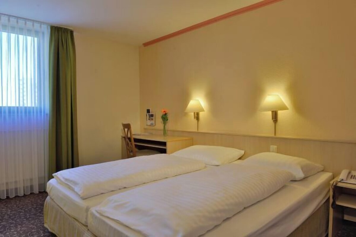A hotel room with two beds, a desk, a chair, lamps, and a telephone.