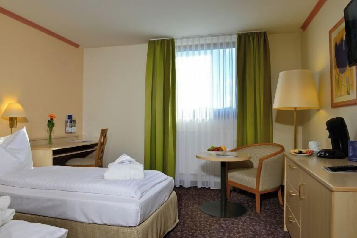 A hotel room with a bed, a desk, a chair, a table, a lamp, a television, and a window with curtains.