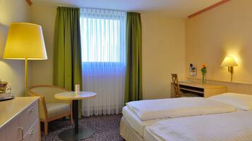 A hotel room with two beds, a desk, a chair, a lamp, and a window with curtains.