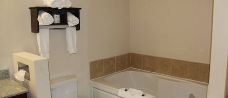 A bathroom with a toilet, a bathtub, and a shelf with towels.