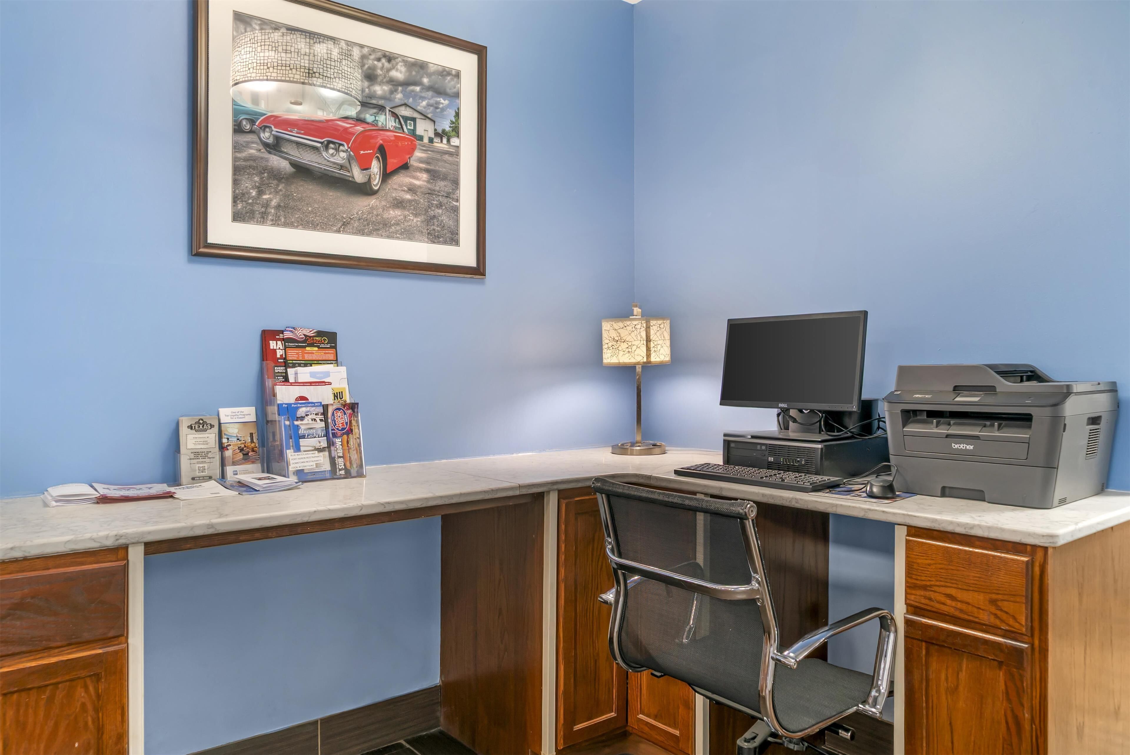 A home office with a desk, computer, printer, and framed picture on the wall.