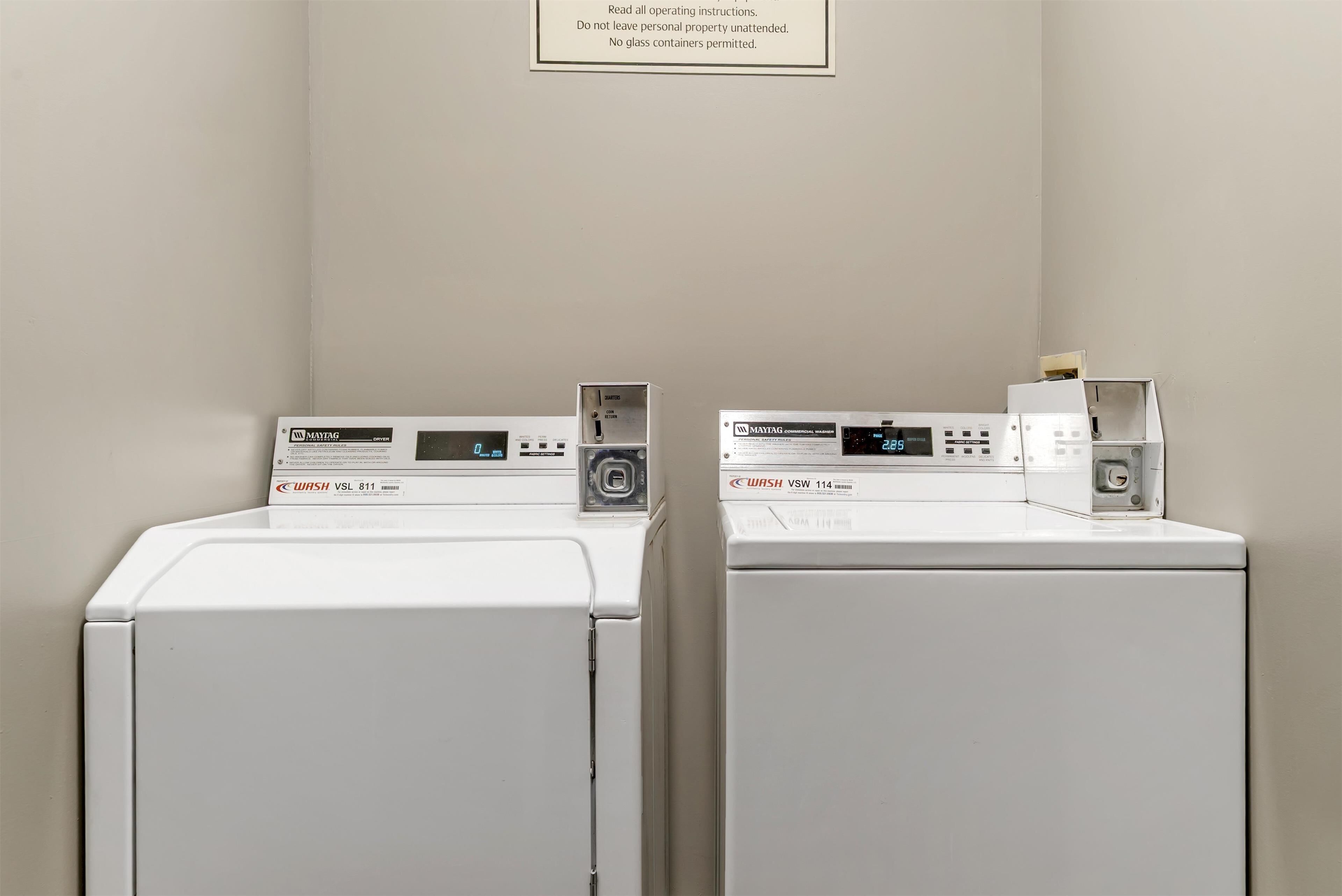 Two front-loading washing machines with control panels, a wall-mounted sign with operating instructions, and a plain wall.