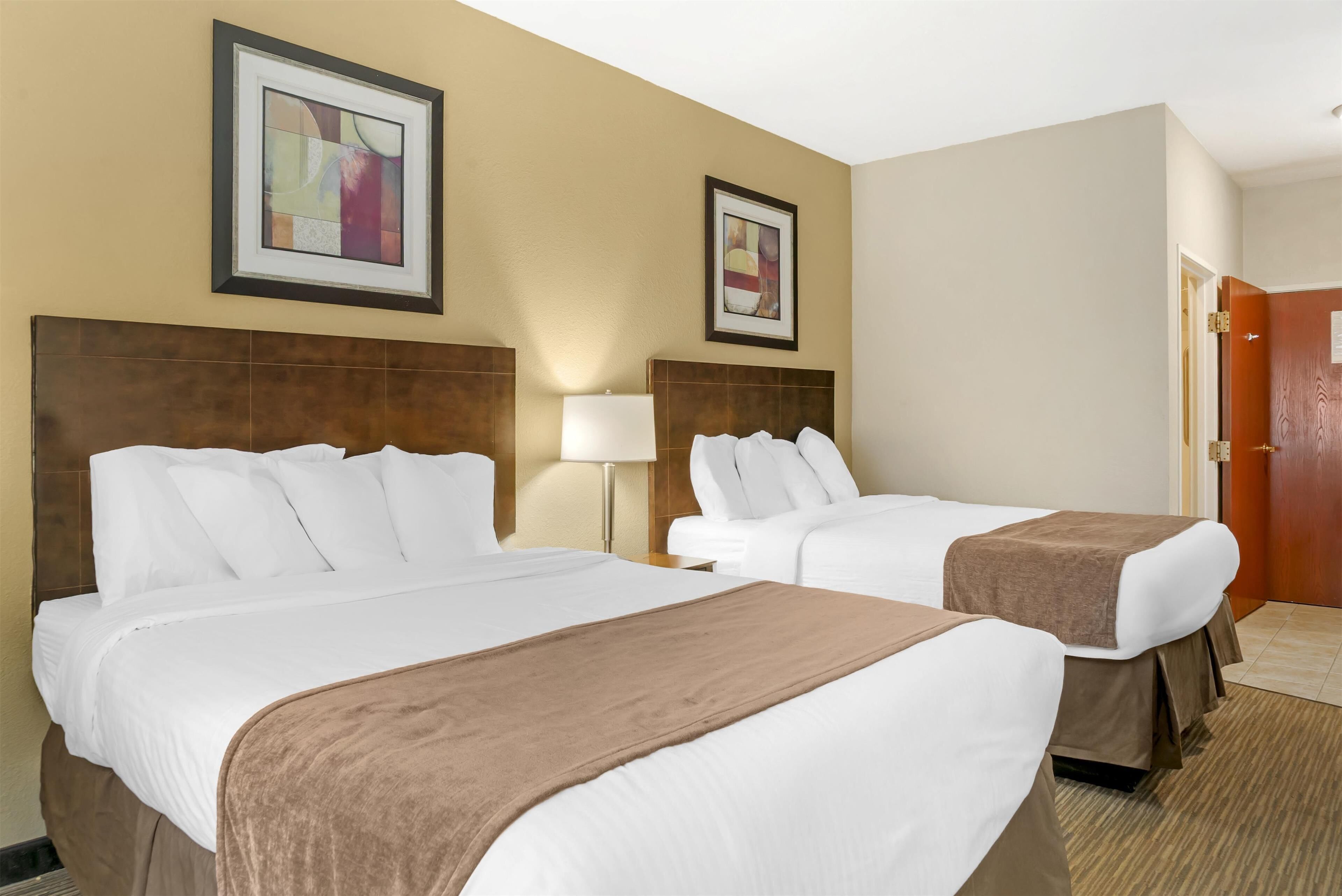 A hotel room with two beds, beige walls, and framed artwork.