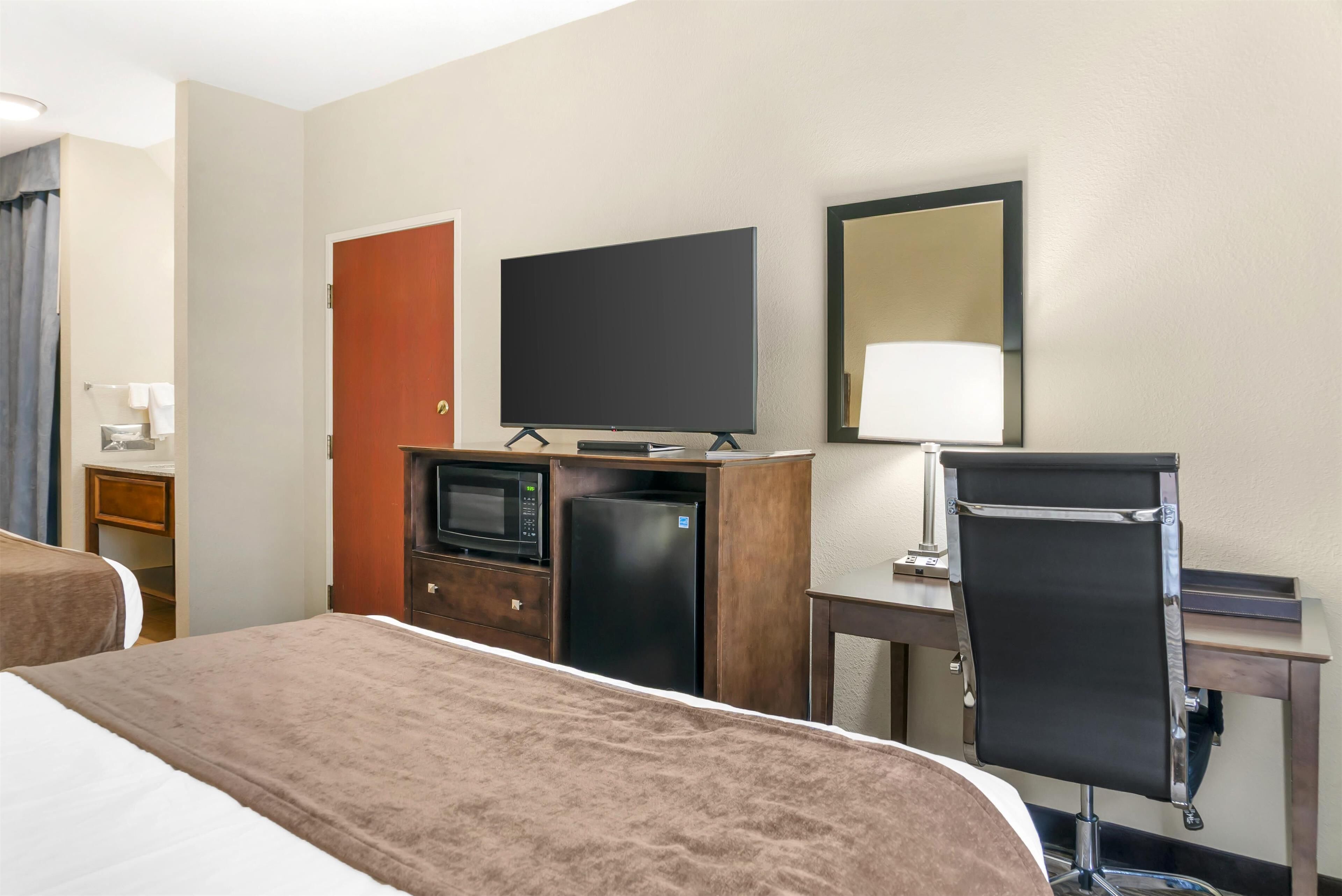A hotel room with a bed, a desk, a television, a refrigerator, and a mirror.
