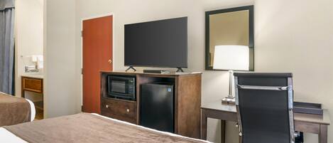A hotel room with a bed, a desk, a television, a refrigerator, and a mirror.
