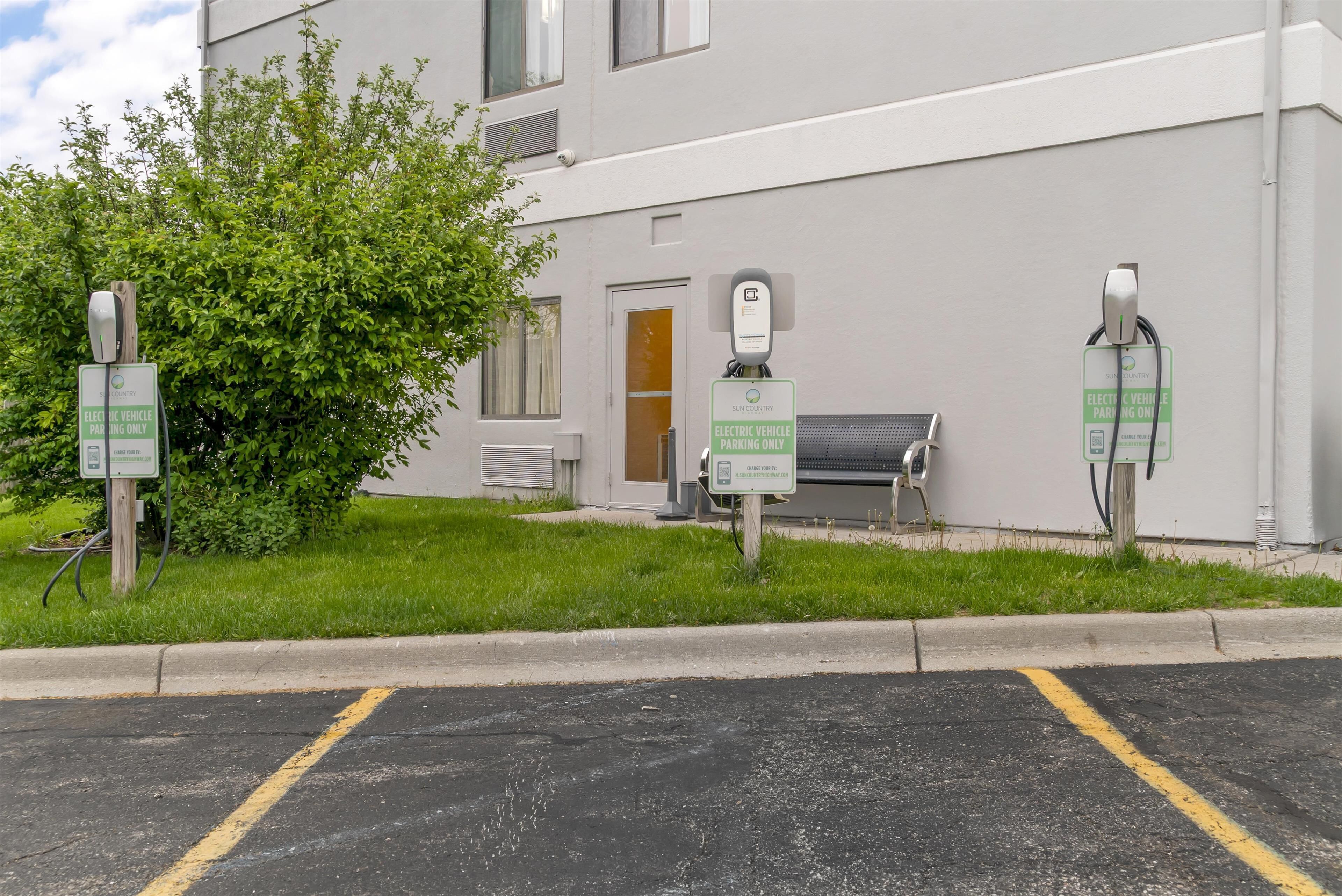 A parking area with electric vehicle charging stations, a bench, and a building with a door and windows.