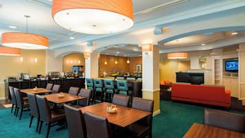 Un vestíbulo de hotel con zona de bar, mesas de comedor y televisor.