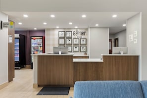 A reception area with a Coca-Cola refrigerator, a check-in counter, and framed artwork on the wall. - Garner Hotel Warren Northwest by IHG (Warren)