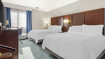 A hotel room with two beds, a desk, a chair, a lamp, and a window with curtains.
