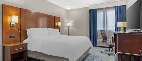 A hotel room with a bed, bedside table, lamp, desk, chair, and a television.