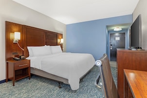 Una habitación de hotel con cama, mesita de noche, lámpara y escritorio con silla.