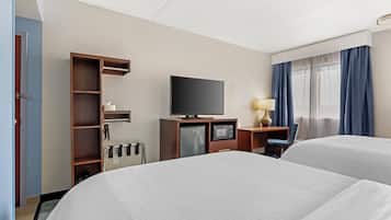 Ett hotellrum med två sängar, en tv, ett skrivbord med en lampa, en minibar och ett fönster med gardiner.