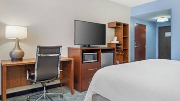 Quarto de hotel com cama, escrivaninha com luminária, cadeira, televisão, micro-ondas e frigorífico.