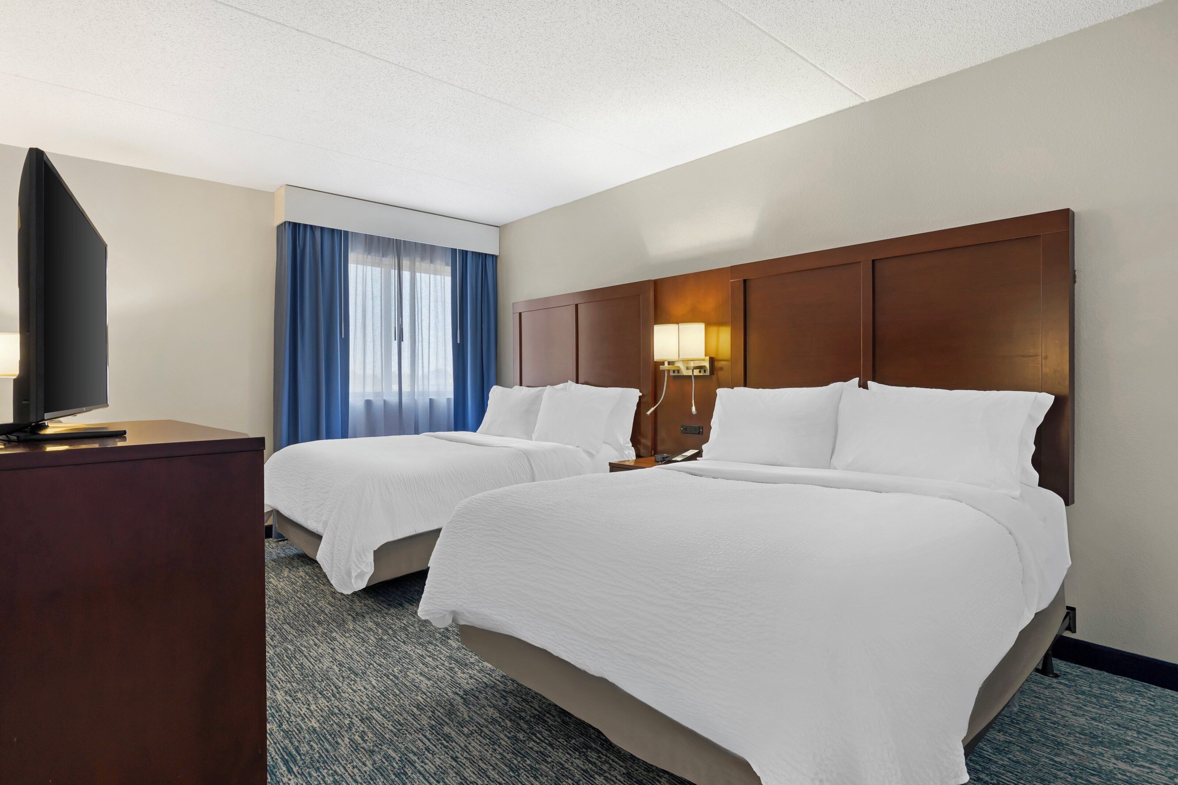 A hotel room with two beds, a flat-screen TV, and a desk.