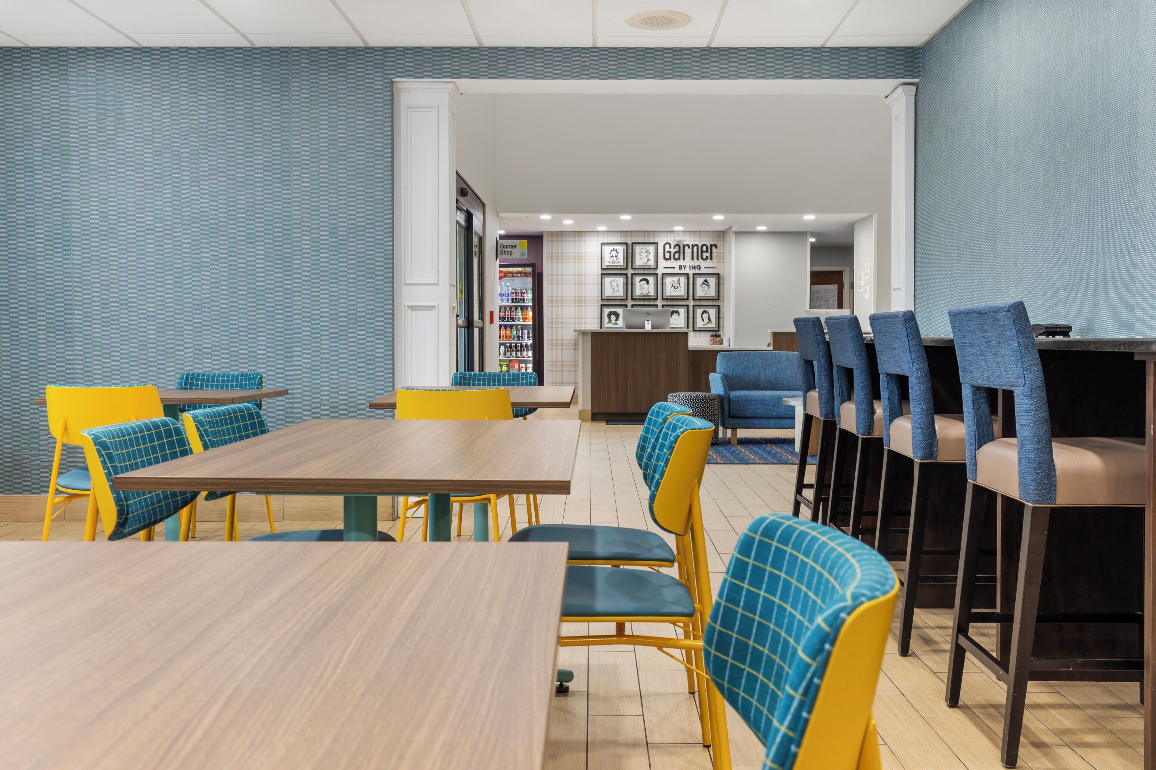 A modern dining area with yellow and blue chairs, a wooden table, and a vending machine.