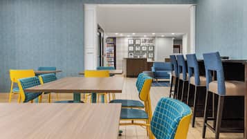 A modern dining area with yellow and blue chairs, a wooden table, and a vending machine.