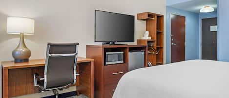 Quarto de hotel com cama, escrivaninha, cadeira, televisão e minibar.