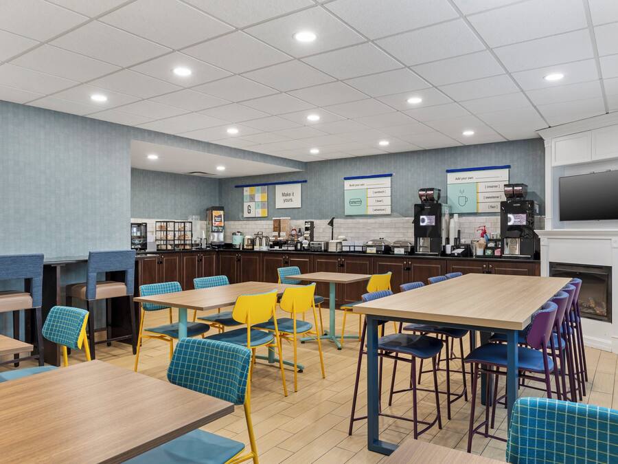 A modern cafeteria with multiple tables and chairs, a coffee station, and a television screen.