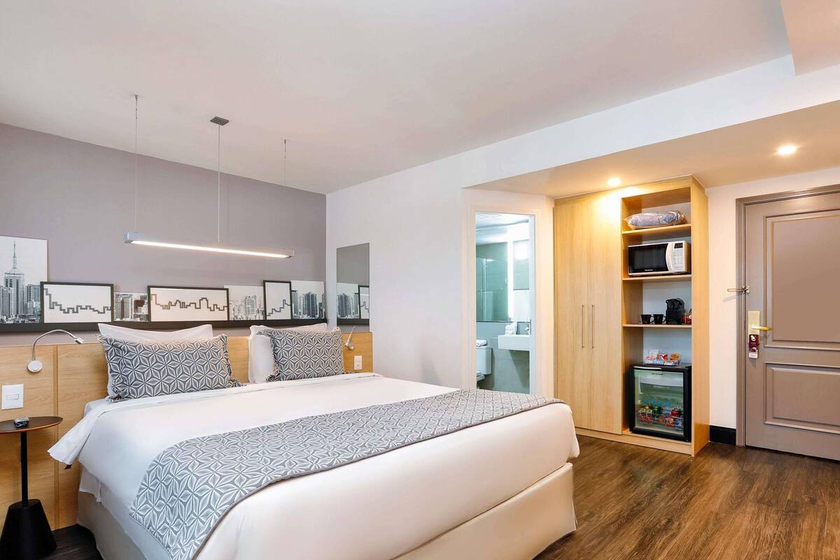 Een moderne hotelkamer met een groot bed, nachtkastjes, een kledingkast en een badkamer die door een open deur zichtbaar is.