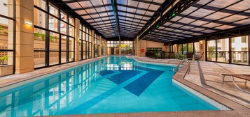 Una piscina interior con agua azul cristalina, rodeada de paredes de azulejos y un techo cubierto.