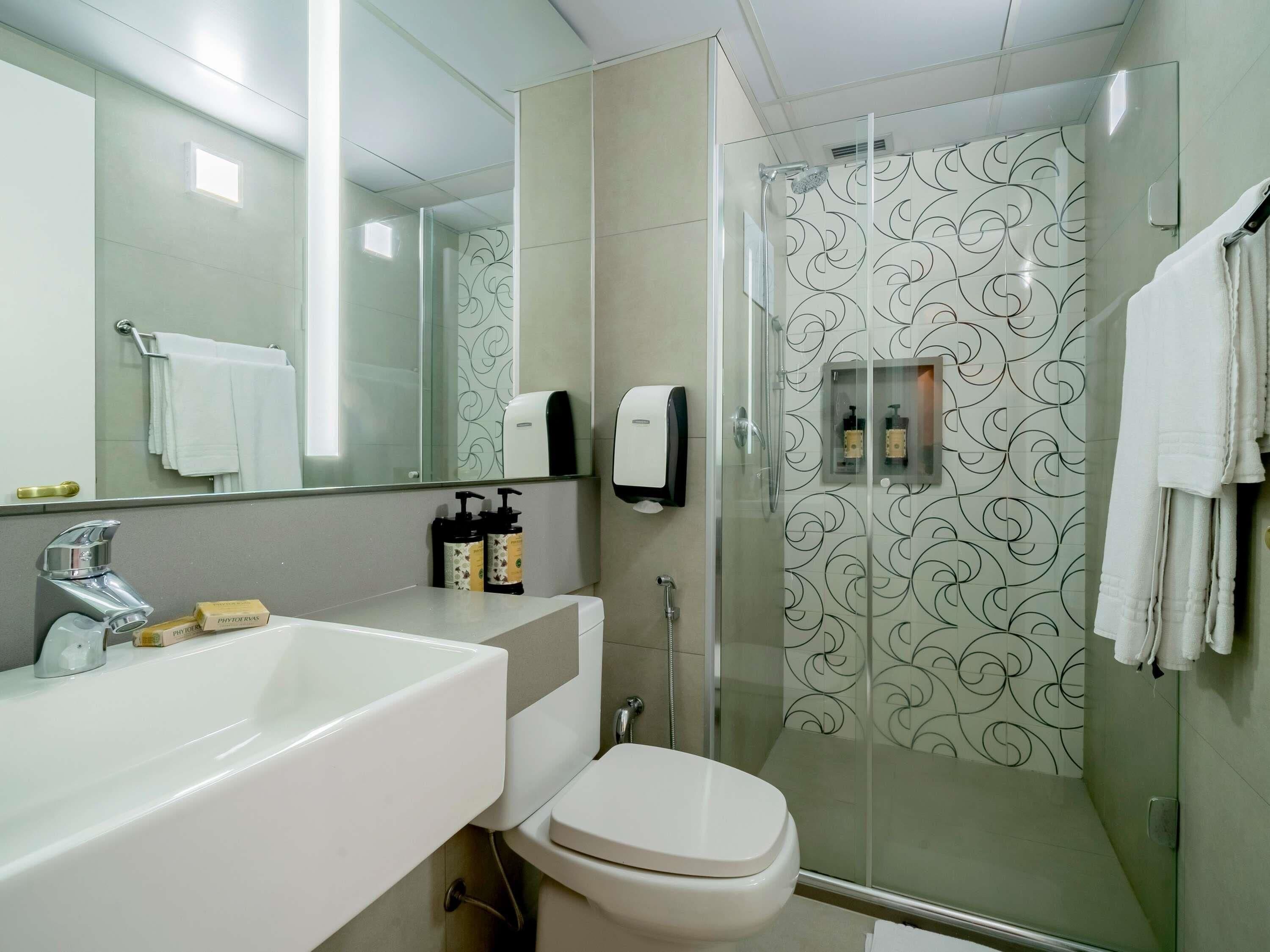 A bathroom with a white sink, a toilet, a glass shower enclosure, and a mirror.