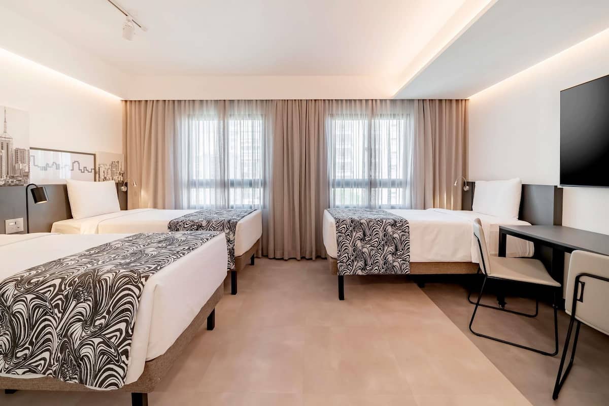 Een hotelkamer met twee bedden, een bureau, een stoel, een televisie en een stadsgezicht schilderij aan de muur.