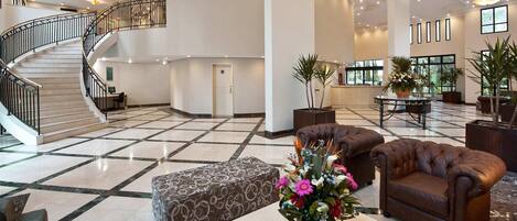 A spacious lobby with a marble floor, a staircase, leather sofas, and potted plants.