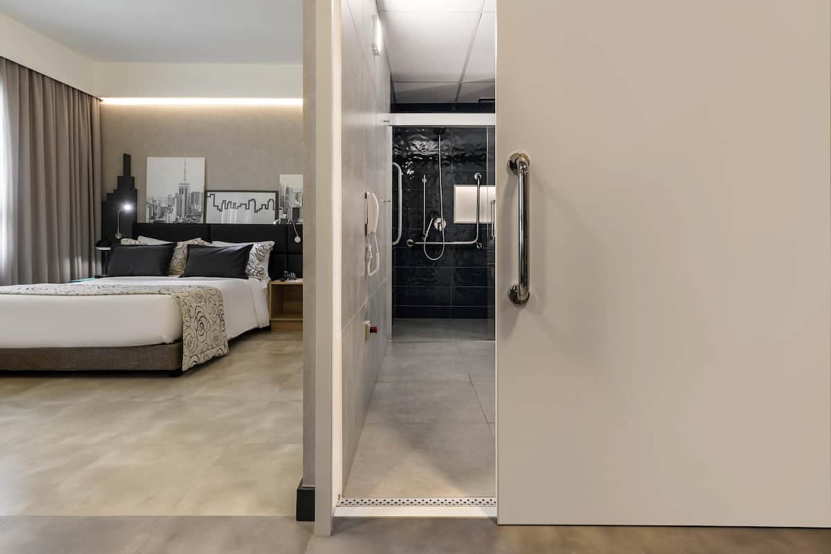 Een moderne hotelkamer met een bed, nachtkastje en een badkamer met douche en toilet.