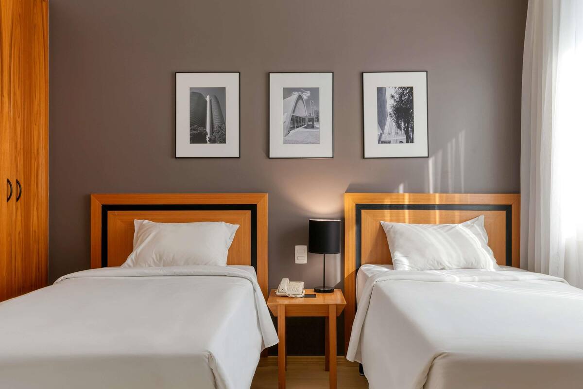 Una habitación de hotel con dos camas, un armario de madera y tres cuadros en la pared.