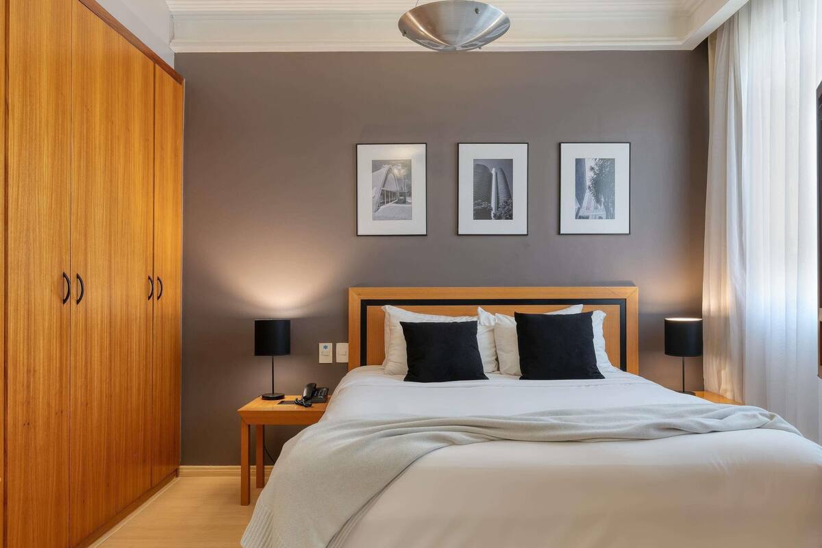 Un cuarto de hotel con una cama grande, un armario de madera y tres cuadros en la pared.