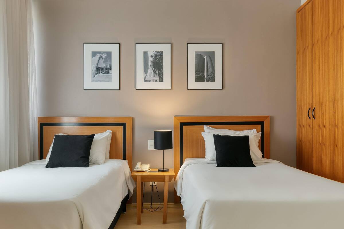 Una habitación de hotel con dos camas, una mesita de noche con lámpara y tres cuadros en la pared.