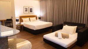 Habitación de hotel con dos camas, un escritorio, una silla, una lámpara y un ventanal grande con cortinas.